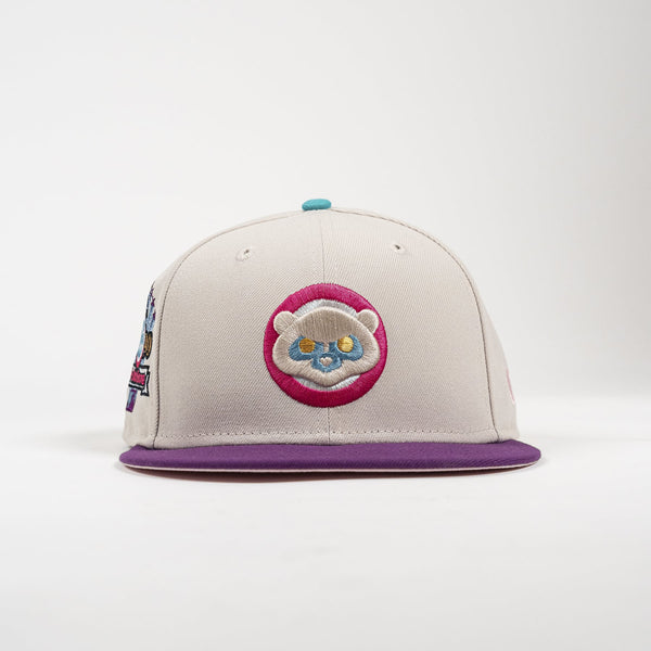 A structured baseball cap in light gray with a purple flat brim, featuring a circular embroidered patch of a cartoon animal face on the front and a small turquoise button on top.