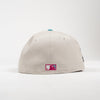 A light beige baseball cap shown from the back, featuring a small rectangular MLB patch on the lower back and a small turquoise button on top, set against a plain white background.