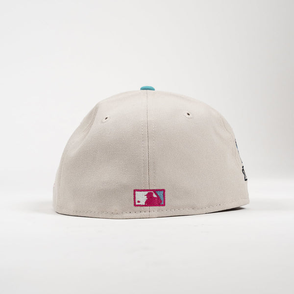 A light beige baseball cap shown from the back, featuring a small rectangular MLB patch on the lower back and a small turquoise button on top, set against a plain white background.