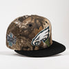 A Philadelphia Eagles 96 Kickoff snapback cap featuring a brown and beige woodland camouflage pattern, a black flat brim, the Philadelphia Eagles logo on the front, and a 35th Anniversary patch on the side.
