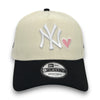 Beige and black cap with New York Yankees logo and pink heart on a white background