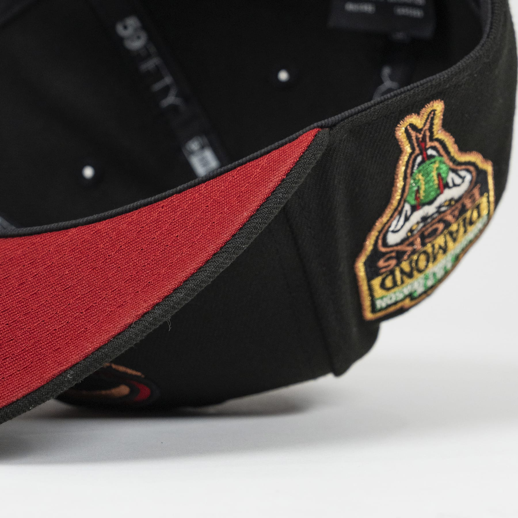Close-up of a black cap with a red interior and embroidered logo on a white background. The Pirates Dbacks 98 59FIFTY Black New Era Hat