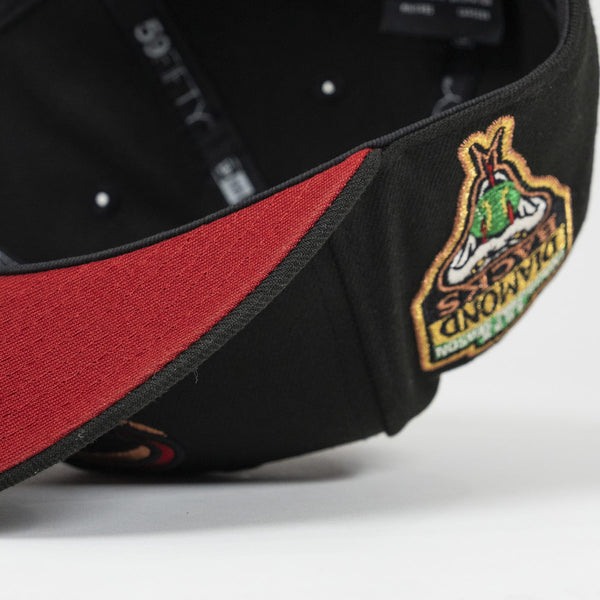 Close-up of a black cap with a red interior and embroidered logo on a white background. The Pirates Dbacks 98 59FIFTY Black New Era Hat